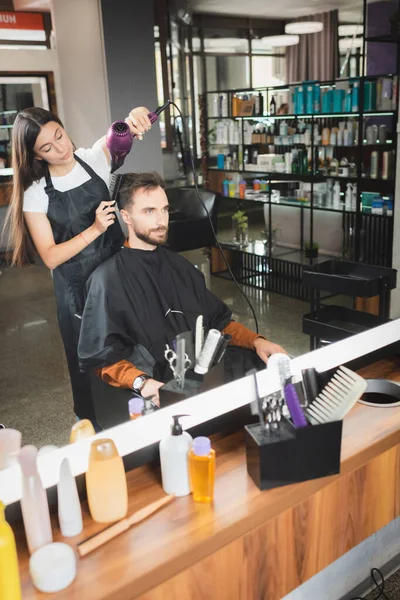 Zrcadlový Odraz Vlasů Vysoušeče Vlasů Klienta Kosmetickými Láhvemi Rozmazaném Popředí — Stock fotografie