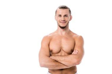 Gülümseyen seksi gömleksiz adam kollarını kavuşturup beyaza yaslanmış şekilde poz veriyor.