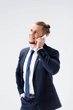 Takım elbiseli gülümseyen genç işadamı, beyaz telefondan izole edilmiş akıllı telefonla konuşuyor.