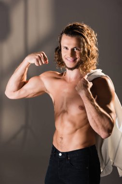 Gülümseyen seksi gömleksiz, uzun saçlı, koyu arkaplanda kaslarını gösteren adam.