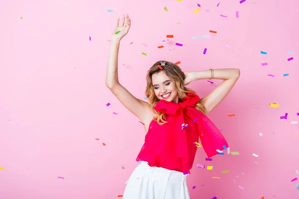 elegant happy woman in crown dancing under confetti on pink background