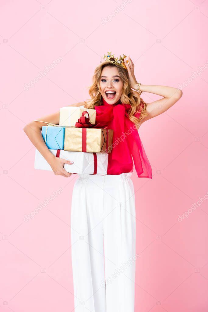 elegant happy woman in crown with gifts on pink background