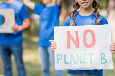 cropped view of girl holding placard with no planet b inscription near mother and father on blurred background clipart