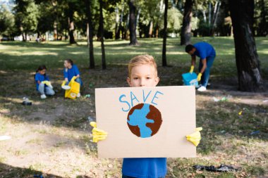 Çocuk elinde kürenin olduğu levhayı tutarken ve yazıyı kaydederken, aile arka planda bulanık plastik atık toplarken, ekoloji konsepti