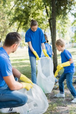 family of activists collecting waste in recycled plastic bags, ecology concept clipart