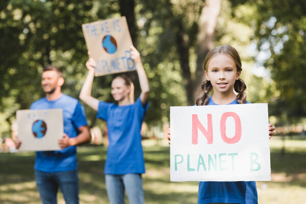girl holding poster with no planet b inscription near parents with placards on blurred background, ecology concept