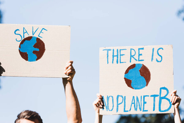 обрезанный вид добровольцев, держащих плакаты с глобусом и нет надписи на планете б на фоне голубого неба, экологическая концепция