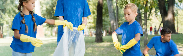 family of volunteers in rubber gloves collecting garbage in recycled bag in forest, ecology concept, banner