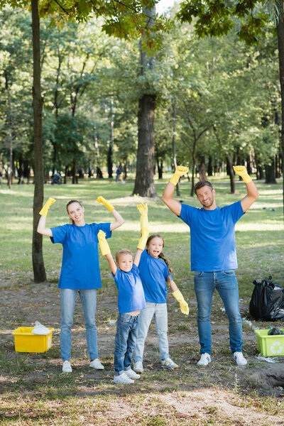 excited family showing success gesture near rubbish containers with plastic waste, ecology concept