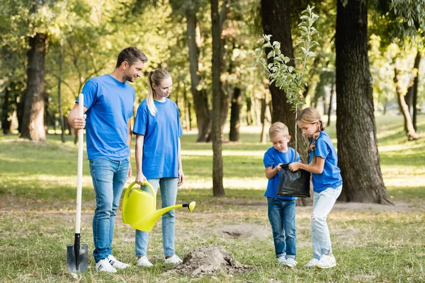 Bambini Che Trasportano Giovani Piantine Vicino Genitori Con Pala Annaffiatoio — Foto Stock