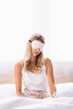 Pijamalı ve göz bandı takmış genç bir kadın. Sabahları yatakta oturuyor. 