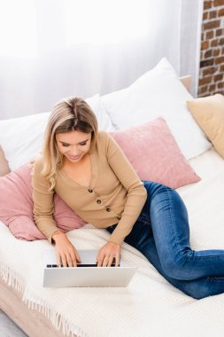 Yatakta yatarken dizüstü bilgisayar kullanan gülümseyen tele-işçi manzarası 