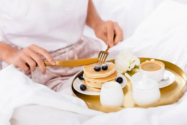 ベッドの上で朝食トレイにベリー コーヒー カーネーションとパンケーキの近くの女性の手の中にカトラリーの作物ビュー — ストック写真