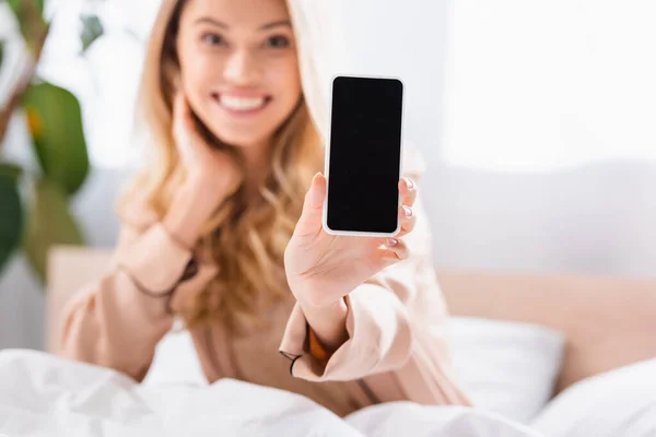 Smartfon Pustym Ekranem Ręku Uśmiechniętej Kobiety Rozmytym Tle Łóżku — Zdjęcie stockowe