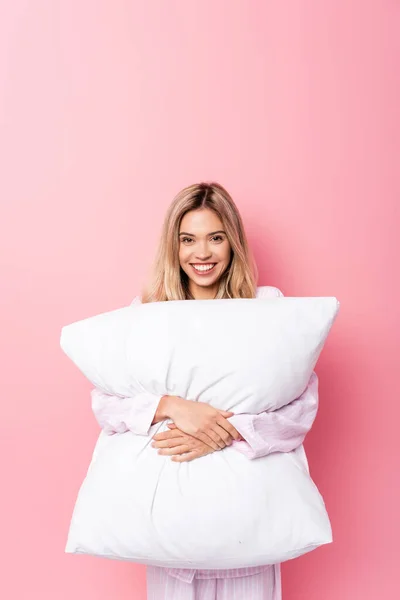 陽気女性でパジャマ保持枕と見てカメラオンピンクの背景 — ストック写真
