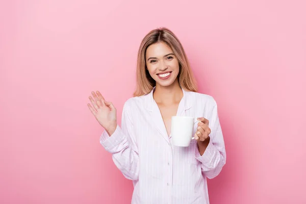 Mujer Sonriente Pijama Sosteniendo Taza Agitando Mano Sobre Fondo Rosa — Foto de Stock