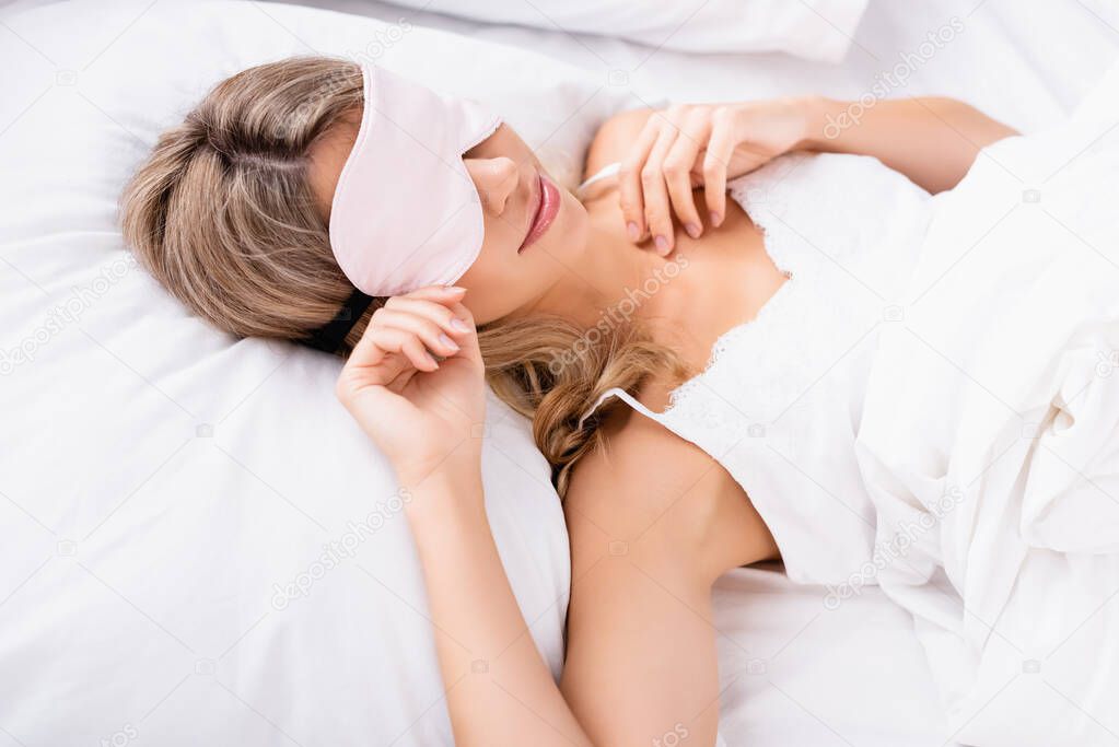 Young woman in blindfold lying on white bedding at morning 