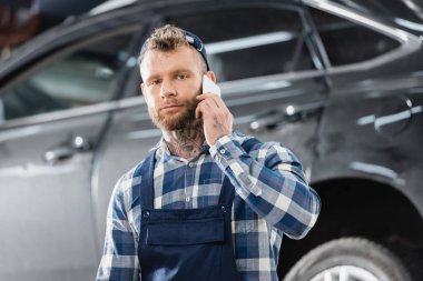 Arkaplanda akıllı telefondan konuşurken kameraya bakan tamirci