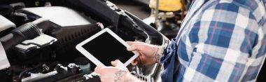 Otomobil motoru kompartımanının yanında dijital tablet tutan tamircinin kısmi görüntüsü, afiş