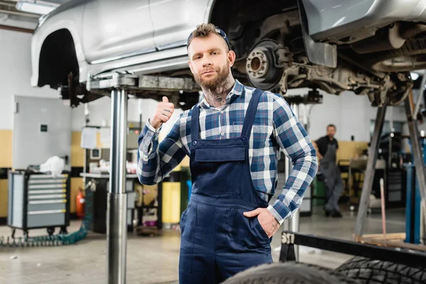 Young Mechanic Showing Thumb While Holding Hand Pocket Raised Car — Stock Photo, Image