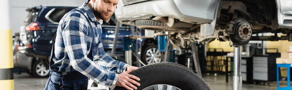 young worker moving car wheel in workshop, banner