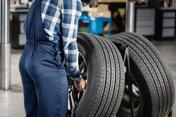 partial view of mechanic in overalls taking car wheel in workshop