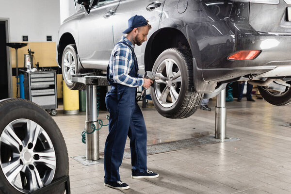 mechanic fixing rear wheel with pneumatic wrench on automobile raised on car lift