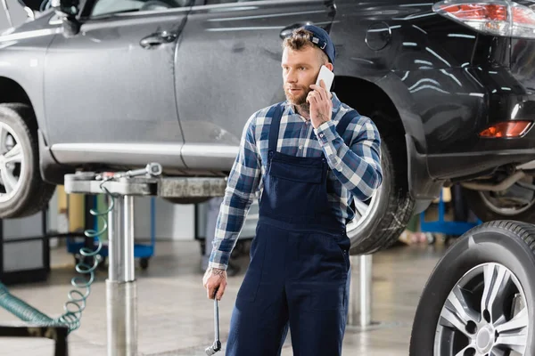 Reparador Segurando Chave Inglesa Falando Telefone Celular Perto Carro Levantado — Fotografia de Stock