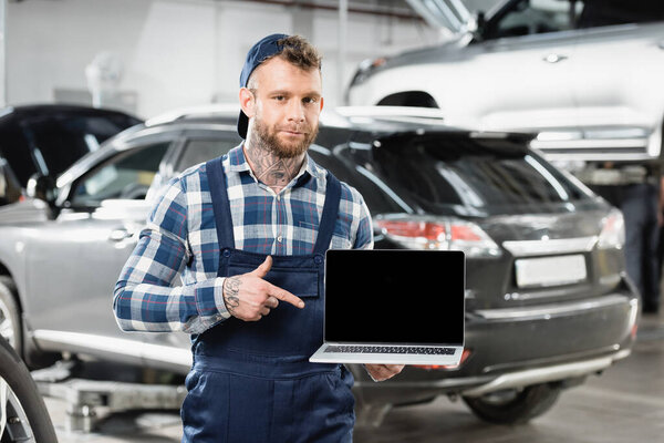 repairman pointing at laptop with blank screen in workshop on blurred background