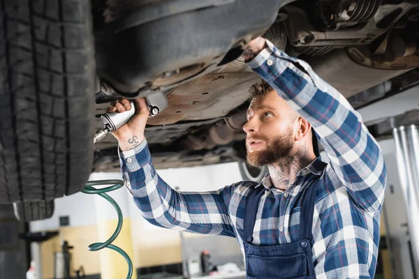 Mladý Technik Opravy Spodní Části Zdviženého Automobilu Pneumatickým Klíčem Rozmazané — Stock fotografie