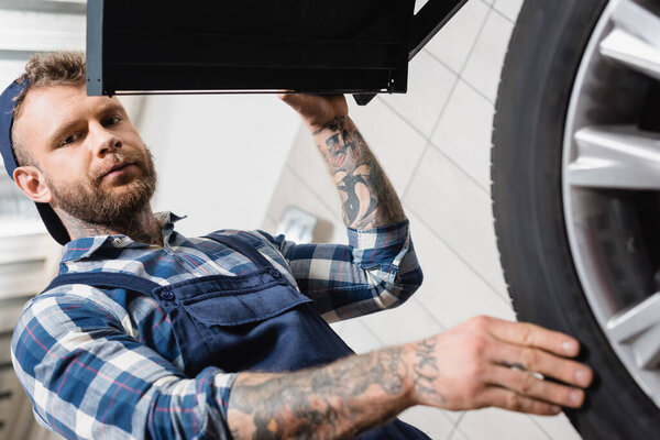 low angle view of technician examining wheel on balance control equipment on blurred foreground