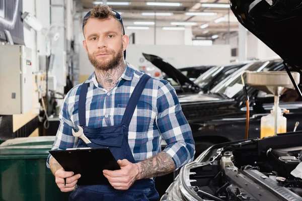 Technikus Kezében Írótábla Mellett Autó Nyitott Motorháztető Kamerába Néz — Stock Fotó