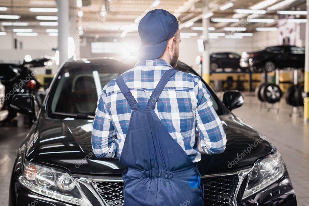 vista posteriore del meccanico in tuta e tappo in piedi in officina vicino alle auto