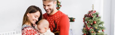 Mutlu ebeveynler kollarında bebek Noel ağacı ve pankartın yanında