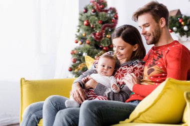 Arkaplanda bulanık noel ağacının yanında kollarında mutlu bir kadın var.