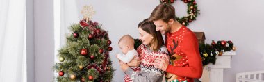 Mutlu bir kadın kucağında kollarıyla neşeli bir koca ve süslü bir Noel ağacı taşıyan bir oğlan çocuğu, afiş