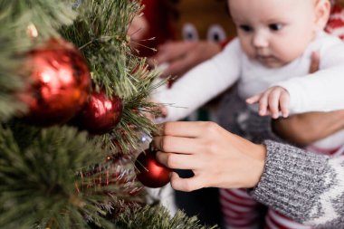 Ön planda noel ağacını süslerken kucağında kolları olan bir kadın. 