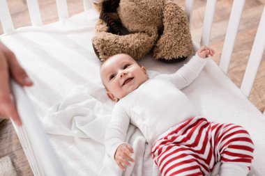 Bebek beşiğinde yatan mutlu çocuk ve bulanık önplanda babasına bakıyor. 