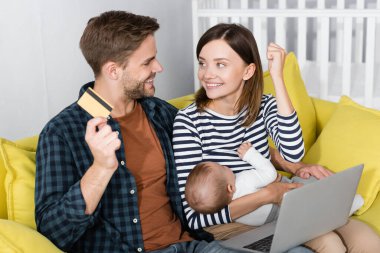 Neşeli bir adam internetten alışveriş yaparken heyecan içindeki karısı ve oğlu yanında kredi kartı tutuyor. 