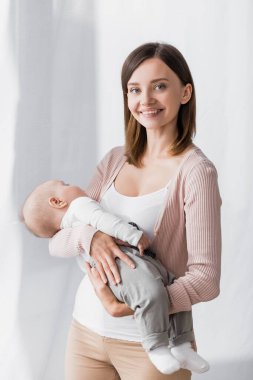 Kollarını tutarken gülümseyen şefkatli kadın uykulu erkek bebek. 