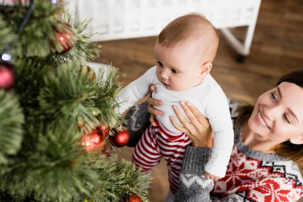 Feliz Mujer Sosteniendo Brazos Bebé Niño Cerca Decorado Árbol Navidad —  Fotos de Stock