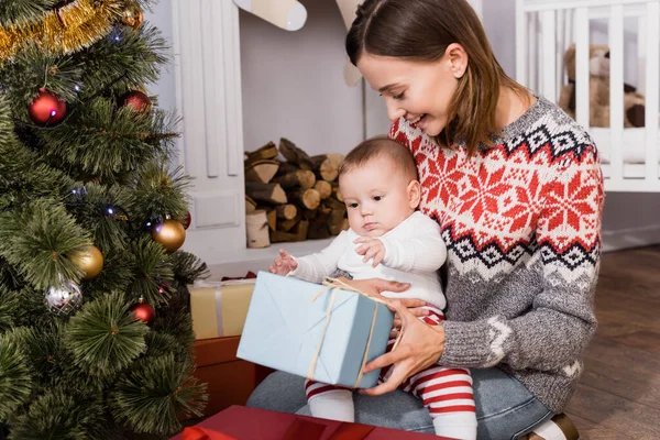 Glückliche Frau Hält Geschenk Neben Baby Und Geschmücktem Weihnachtsbaum — Stockfoto