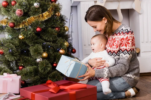 Gülümseyen Bir Kadın Bebeğinin Yanında Hediyesini Tutuyor Noel Ağacını Süslüyor — Stok fotoğraf