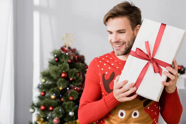 Uomo Allegro Maglione Tenuta Avvolto Presente Vicino Albero Natale Sfondo — Foto Stock