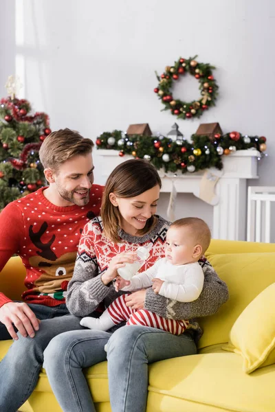 Happy Mother Feeding Infant Son Husband Christmas Tree Blurred Background — Stock Photo, Image