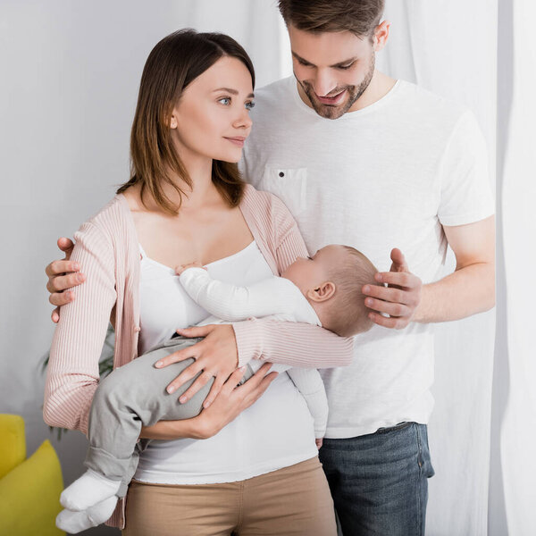 woman holding in arms infant boy near caring husband 