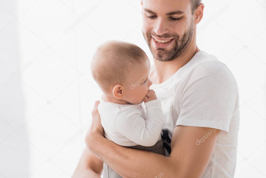 cheerful father holding in arms baby boy sucking fingers 