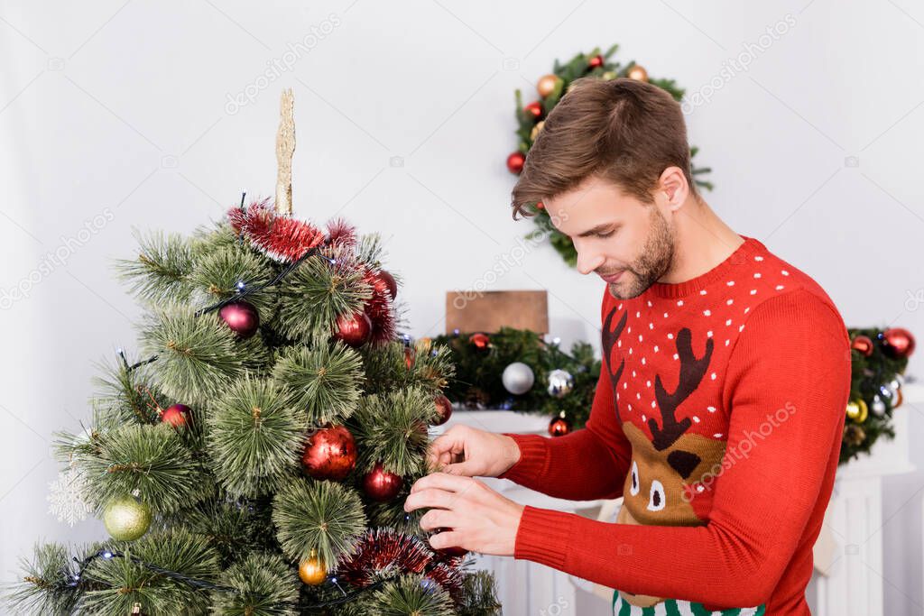 bearded man in sweater decorating christmas tree at home
