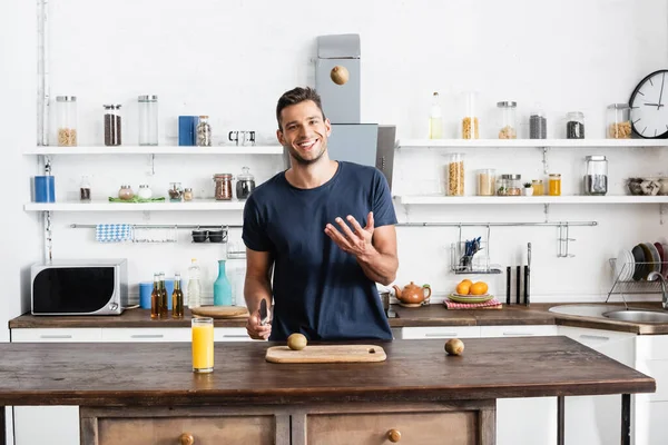 Uomo Sorridente Gettando Kiwi Mentre Tiene Coltello Vicino Tagliere Vetro — Foto Stock