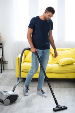 Oturma odasında elektrik süpürgesi kullanan bir adam. 